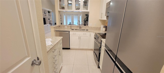 kitchen featuring appliances with stainless steel finishes, white cabinetry, sink, light tile patterned floors, and light stone countertops