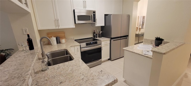 kitchen featuring appliances with stainless steel finishes, light tile patterned flooring, white cabinets, a sink, and light stone countertops