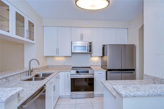 kitchen with light stone counters, a sink, white cabinets, appliances with stainless steel finishes, and glass insert cabinets