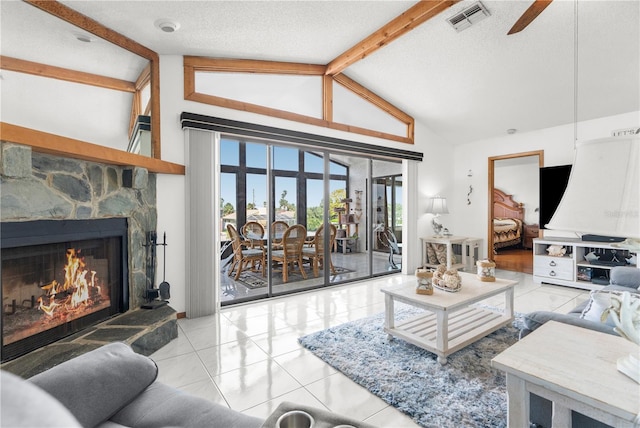 living room featuring beamed ceiling, ceiling fan, a stone fireplace, light tile patterned flooring, and a textured ceiling