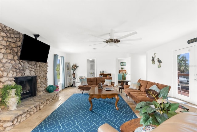 living room with ceiling fan, light tile patterned floors, and a stone fireplace