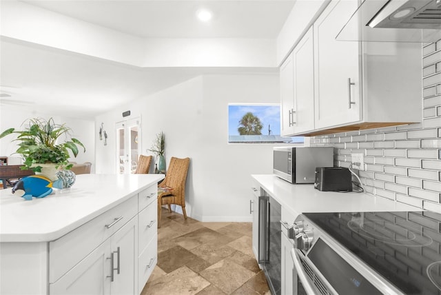 kitchen with ventilation hood, white cabinets, stainless steel appliances, and decorative backsplash