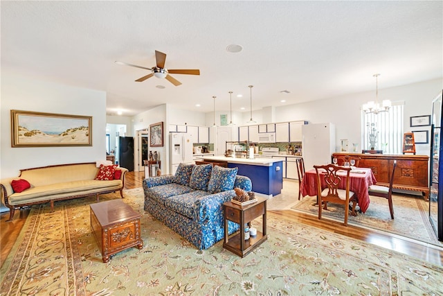 living room featuring ceiling fan with notable chandelier and light hardwood / wood-style flooring