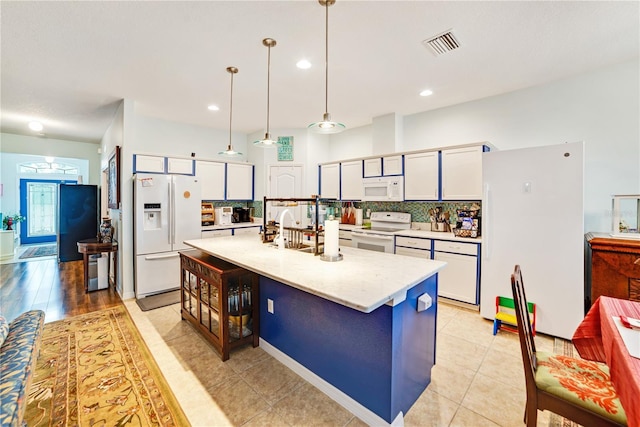 kitchen with white appliances, pendant lighting, light tile patterned floors, white cabinetry, and an island with sink