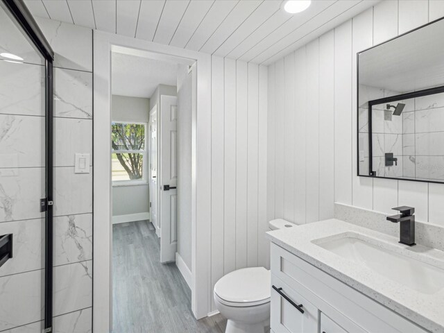 bathroom with a shower with shower door, wood walls, vanity, hardwood / wood-style flooring, and toilet