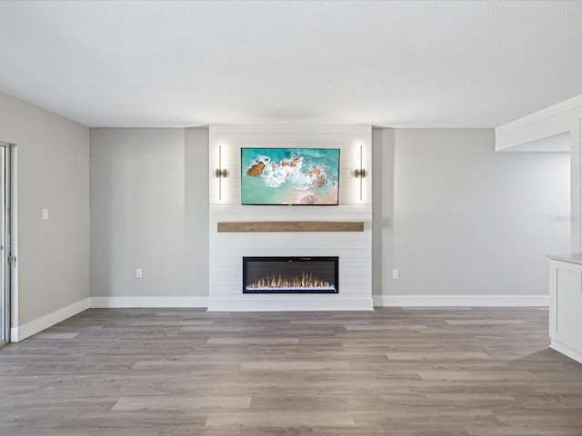 unfurnished living room with a textured ceiling, light hardwood / wood-style flooring, and a large fireplace