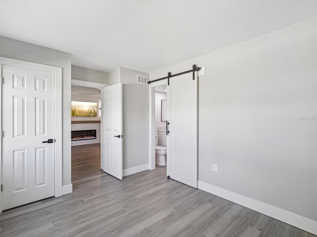 unfurnished bedroom with a barn door, light hardwood / wood-style floors, and ensuite bathroom