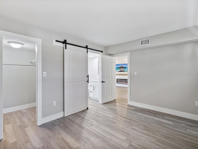 unfurnished bedroom featuring a closet, light hardwood / wood-style flooring, a barn door, and a spacious closet