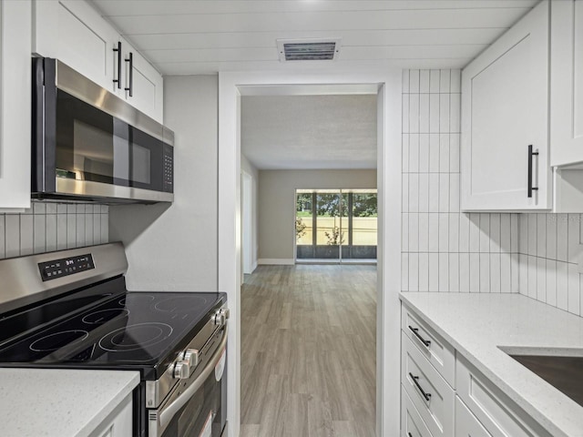 kitchen with white cabinets, appliances with stainless steel finishes, light stone countertops, and light hardwood / wood-style flooring