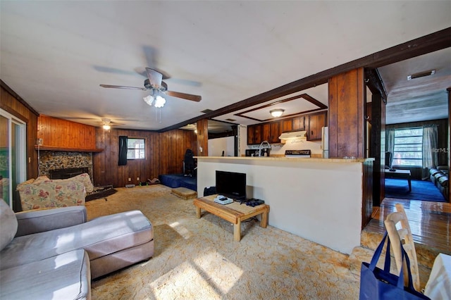 carpeted living room featuring ceiling fan, a fireplace, wood walls, and ornamental molding