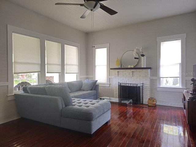 living room featuring a fireplace, ceiling fan, dark wood-type flooring, and brick wall