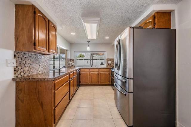 kitchen with appliances with stainless steel finishes, tasteful backsplash, dark stone counters, a textured ceiling, and light tile patterned floors