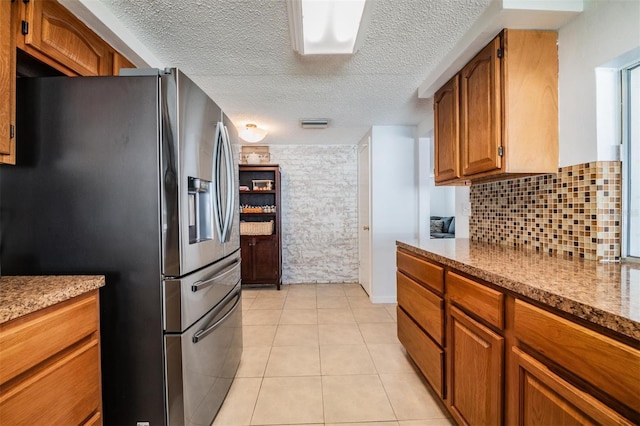 kitchen featuring tasteful backsplash, stainless steel fridge, light tile patterned floors, and a textured ceiling