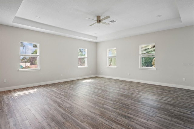 empty room featuring a raised ceiling, dark wood-type flooring, and ceiling fan