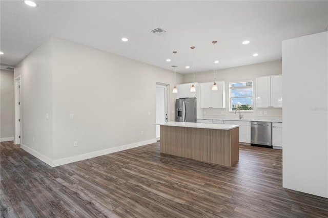 kitchen with hanging light fixtures, a kitchen island, white cabinetry, appliances with stainless steel finishes, and dark hardwood / wood-style flooring