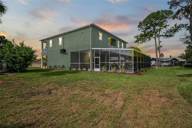 back house at dusk featuring a sunroom and a yard