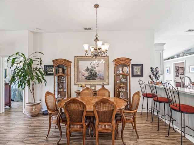 dining area with wood-type flooring, a notable chandelier, and sink