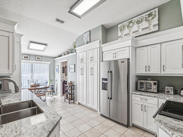 kitchen featuring high end refrigerator, vaulted ceiling, white cabinetry, light tile patterned floors, and sink