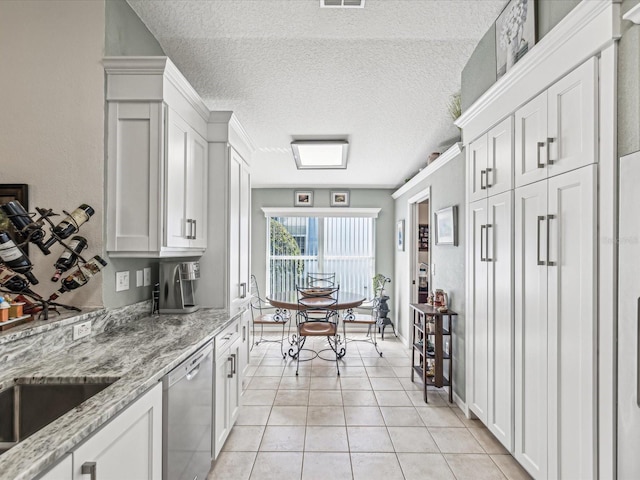 kitchen with white cabinetry, light stone counters, dishwasher, light tile patterned floors, and a textured ceiling