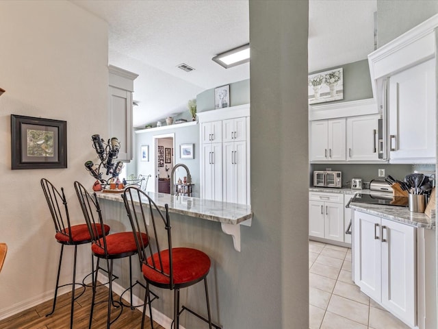 kitchen featuring a kitchen breakfast bar, light hardwood / wood-style floors, white cabinetry, kitchen peninsula, and light stone countertops