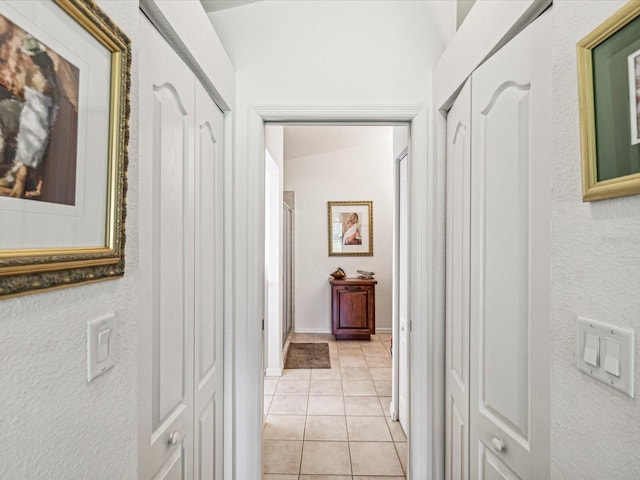 corridor with light tile patterned flooring and vaulted ceiling