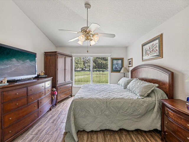 bedroom with access to outside, ceiling fan, light hardwood / wood-style floors, a textured ceiling, and vaulted ceiling