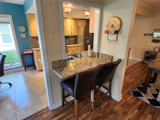 kitchen featuring a breakfast bar, light stone counters, stainless steel fridge with ice dispenser, backsplash, and hardwood / wood-style floors