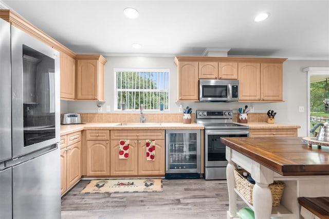 kitchen with ornamental molding, appliances with stainless steel finishes, beverage cooler, and light brown cabinetry