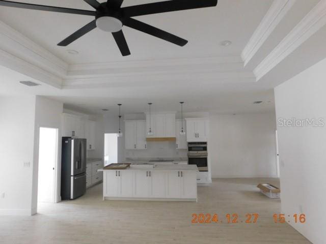 kitchen with a raised ceiling, stainless steel fridge, a center island, and white cabinets