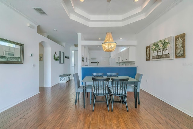 dining area with wood-type flooring, an inviting chandelier, a tray ceiling, and ornamental molding