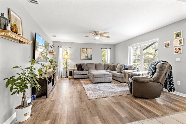 living area featuring a textured ceiling, ceiling fan, wood finished floors, and baseboards