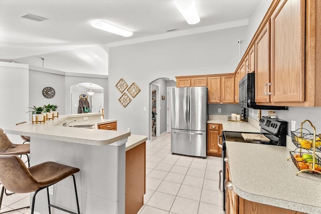 kitchen featuring arched walkways, light countertops, appliances with stainless steel finishes, and a kitchen breakfast bar