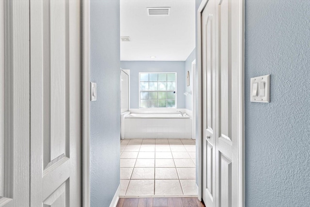 hall featuring tile patterned flooring, visible vents, and a textured wall