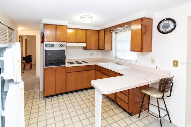 kitchen with white gas cooktop, a breakfast bar, a textured ceiling, oven, and sink