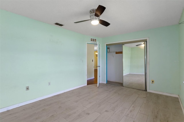 unfurnished bedroom with light wood-type flooring, a textured ceiling, ceiling fan, and a closet