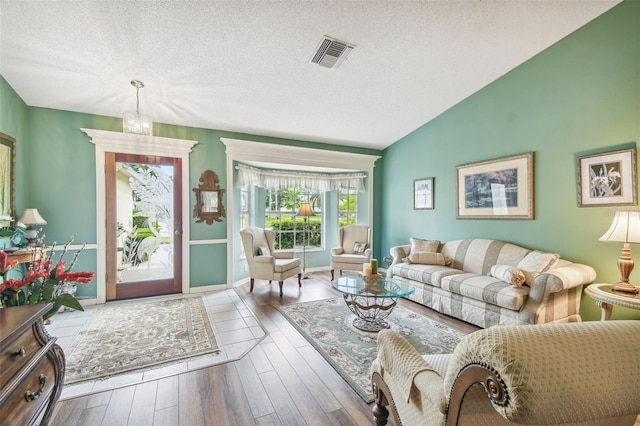 living room with wood-type flooring, a textured ceiling, an inviting chandelier, and vaulted ceiling