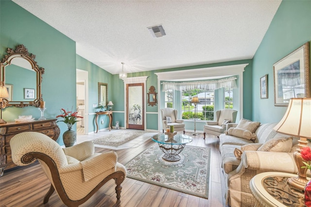 living room with hardwood / wood-style floors, an inviting chandelier, vaulted ceiling, and a textured ceiling