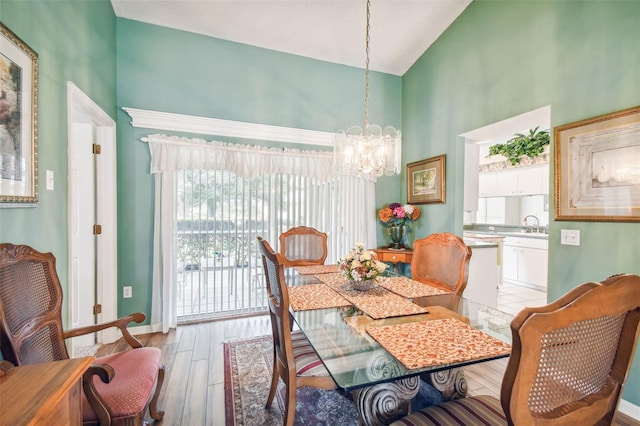 dining room featuring high vaulted ceiling, sink, light wood-type flooring, and an inviting chandelier