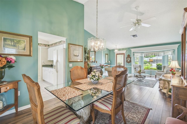 dining area featuring high vaulted ceiling, light wood-type flooring, and ceiling fan with notable chandelier