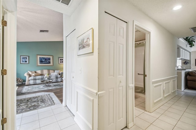 corridor with lofted ceiling, a textured ceiling, and light tile patterned floors