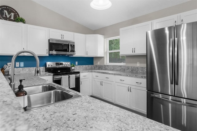 kitchen featuring appliances with stainless steel finishes, vaulted ceiling, white cabinetry, light stone countertops, and sink