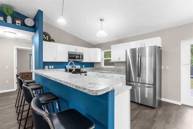 kitchen with pendant lighting, lofted ceiling, a kitchen breakfast bar, appliances with stainless steel finishes, and dark hardwood / wood-style flooring