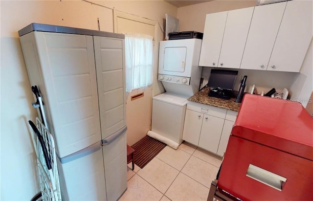 kitchen with dark stone counters, stacked washing maching and dryer, light tile patterned flooring, and white cabinets