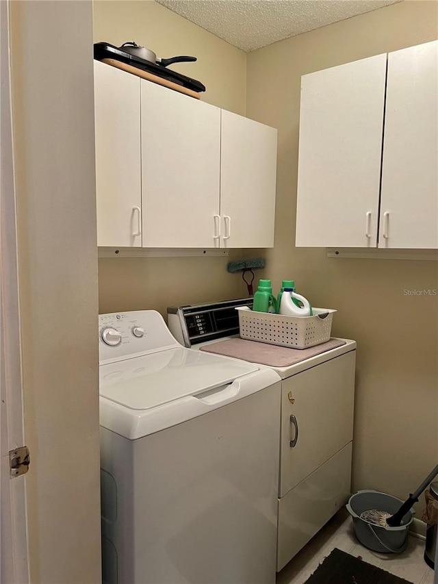 laundry room featuring cabinets, a textured ceiling, and washer and clothes dryer