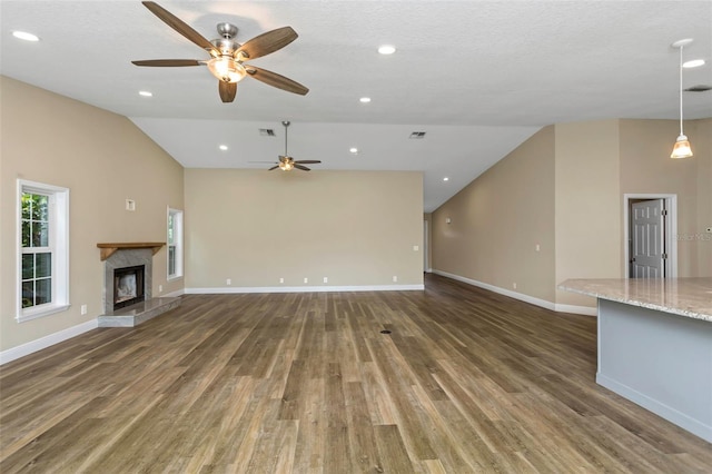 unfurnished living room with dark wood-type flooring, vaulted ceiling, a premium fireplace, a textured ceiling, and ceiling fan