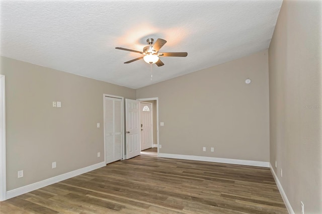 spare room with dark wood-type flooring, a textured ceiling, vaulted ceiling, and ceiling fan