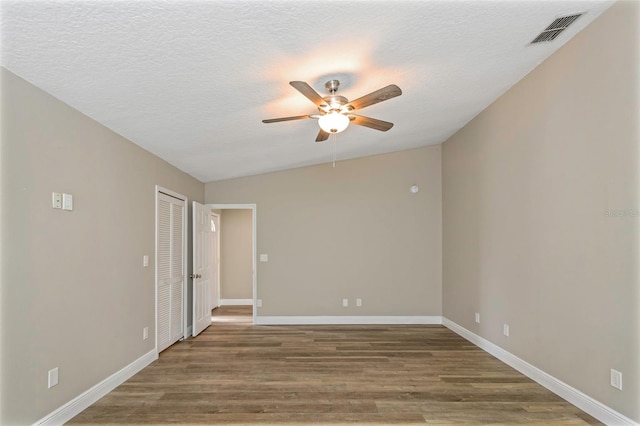 empty room featuring lofted ceiling, hardwood / wood-style floors, ceiling fan, and a textured ceiling