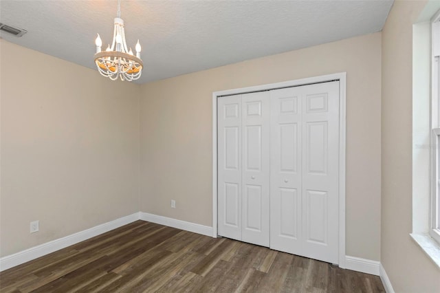 unfurnished bedroom with dark hardwood / wood-style floors, a textured ceiling, a chandelier, and a closet