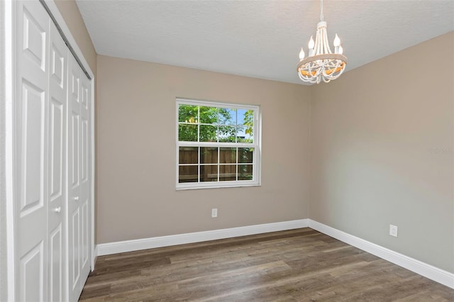 unfurnished bedroom with a textured ceiling, dark wood-type flooring, a chandelier, and a closet