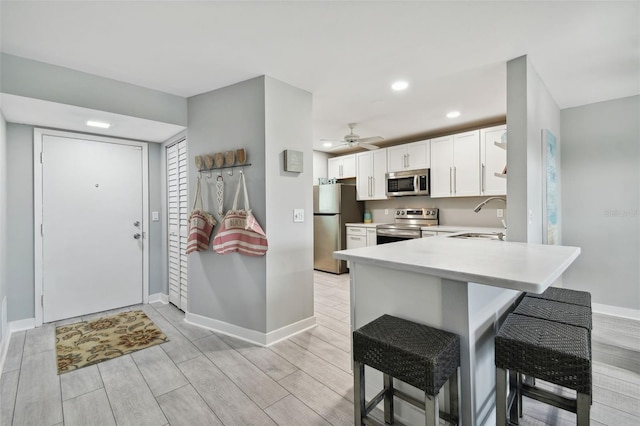 kitchen featuring kitchen peninsula, stainless steel appliances, a kitchen bar, ceiling fan, and sink